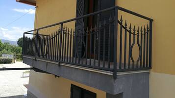 Een balkon met een sierijzeren hekwerk, een raam met luiken en een klein buiten terrasje met een bloempot.