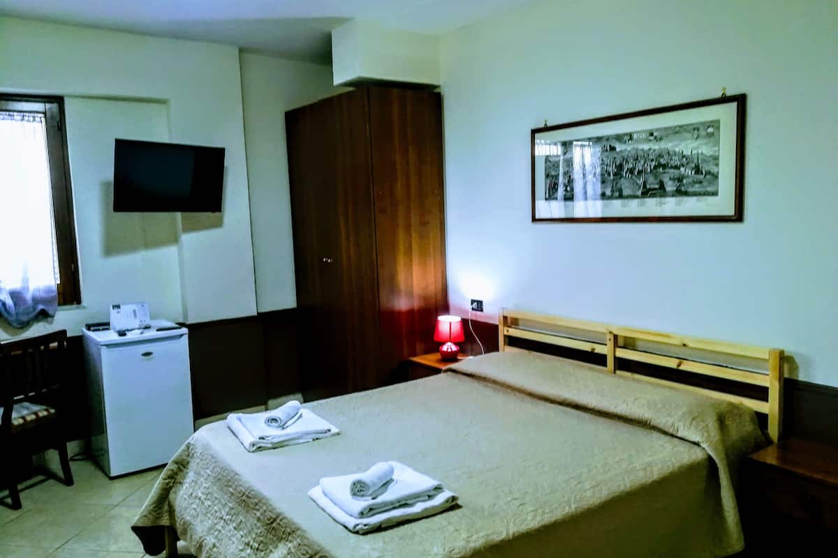 A hotel room with a bed, a desk with a computer, a television, a wardrobe, and a framed picture on the wall.