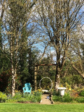 Un jardín con un columpio, una silla azul y una maceta blanca.