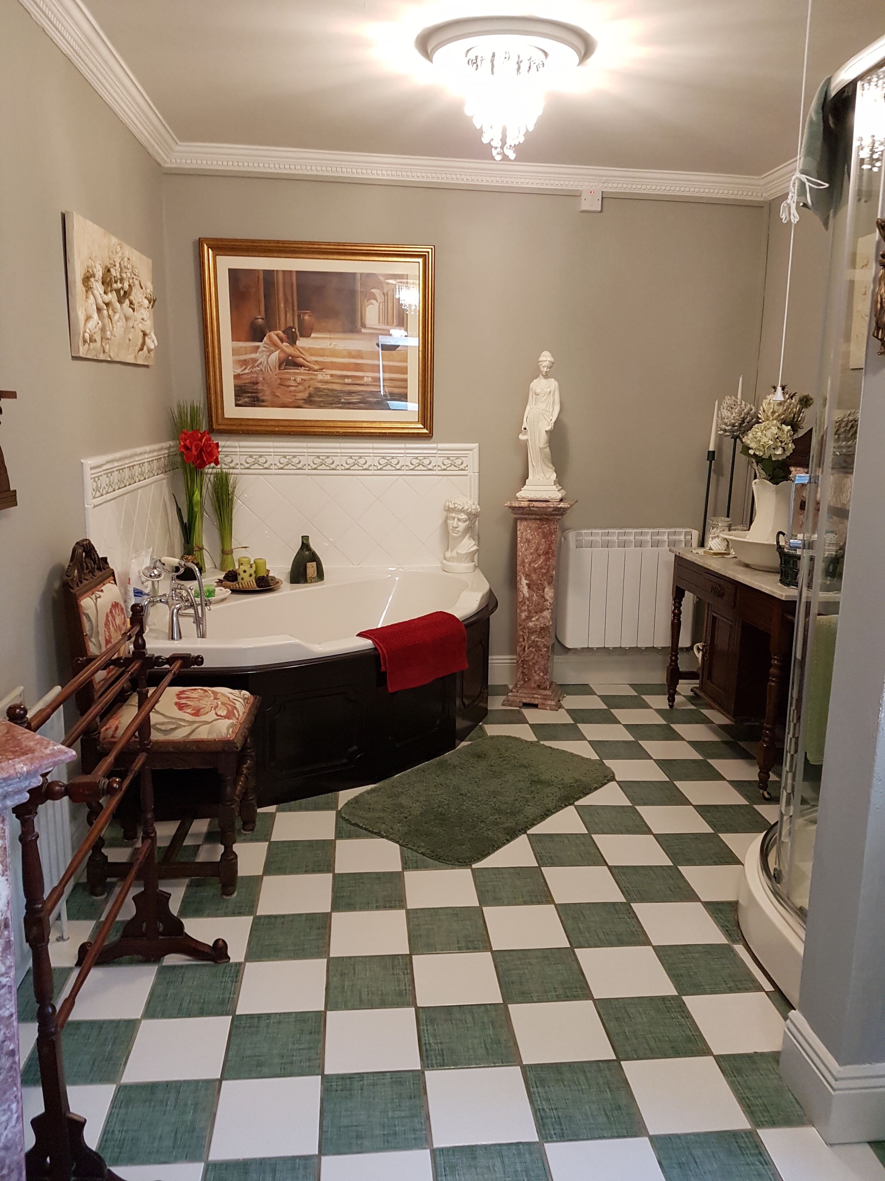 Un baño con piso a cuadros, una bañera, un tocador con espejo y una estatua.