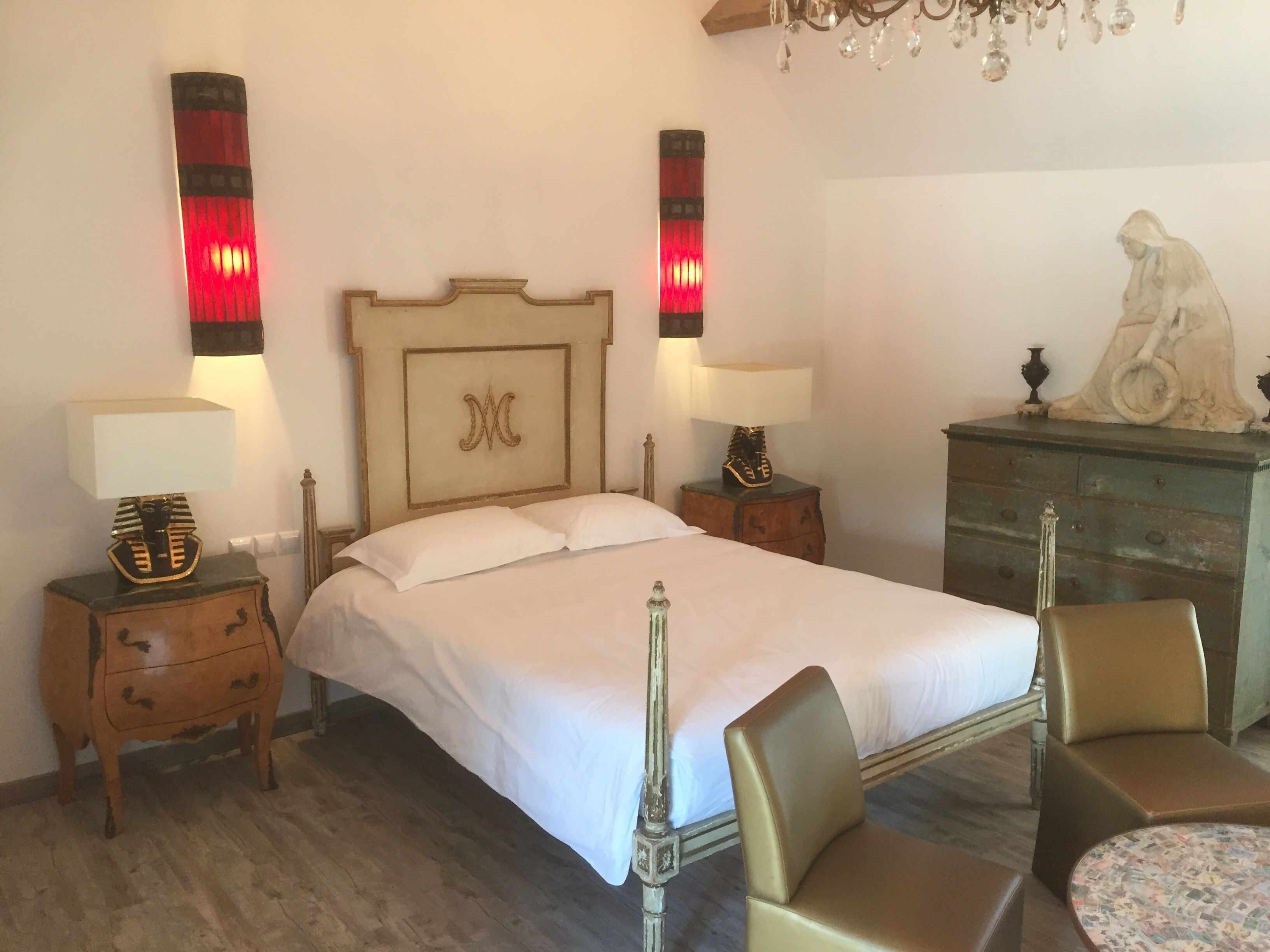 A bedroom with a bed, two bedside tables with lamps, a dresser, a chair, and a statue on the dresser.
