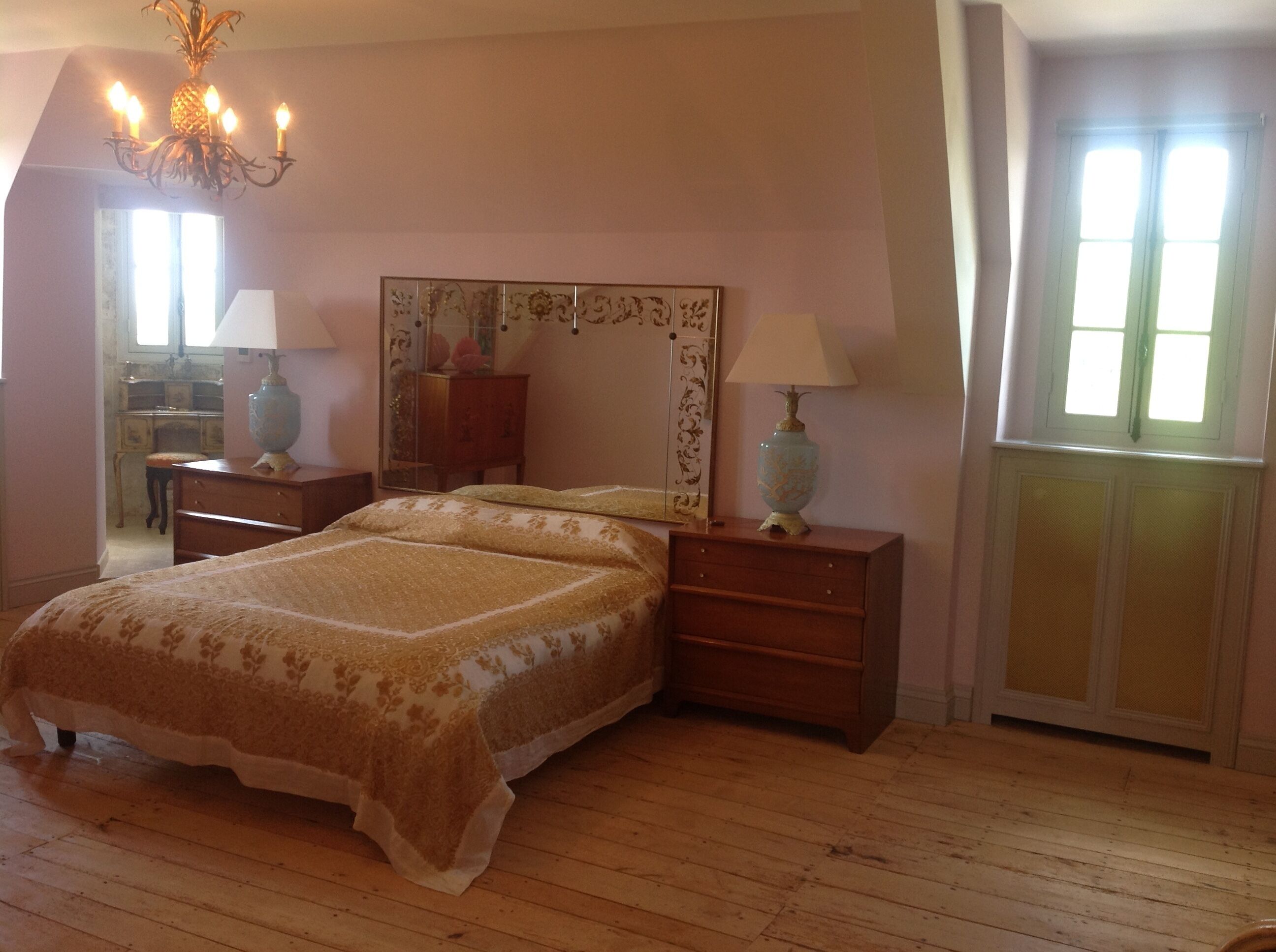 Un dormitorio con cama, mesitas de noche, cómoda, espejo y una araña.