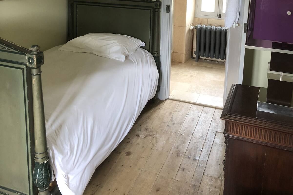 Ein Schlafzimmer mit einem hölzernen Bett, einem Schminktisch, einer Pendelleuchte und einer Tür zu einem weiteren Raum.