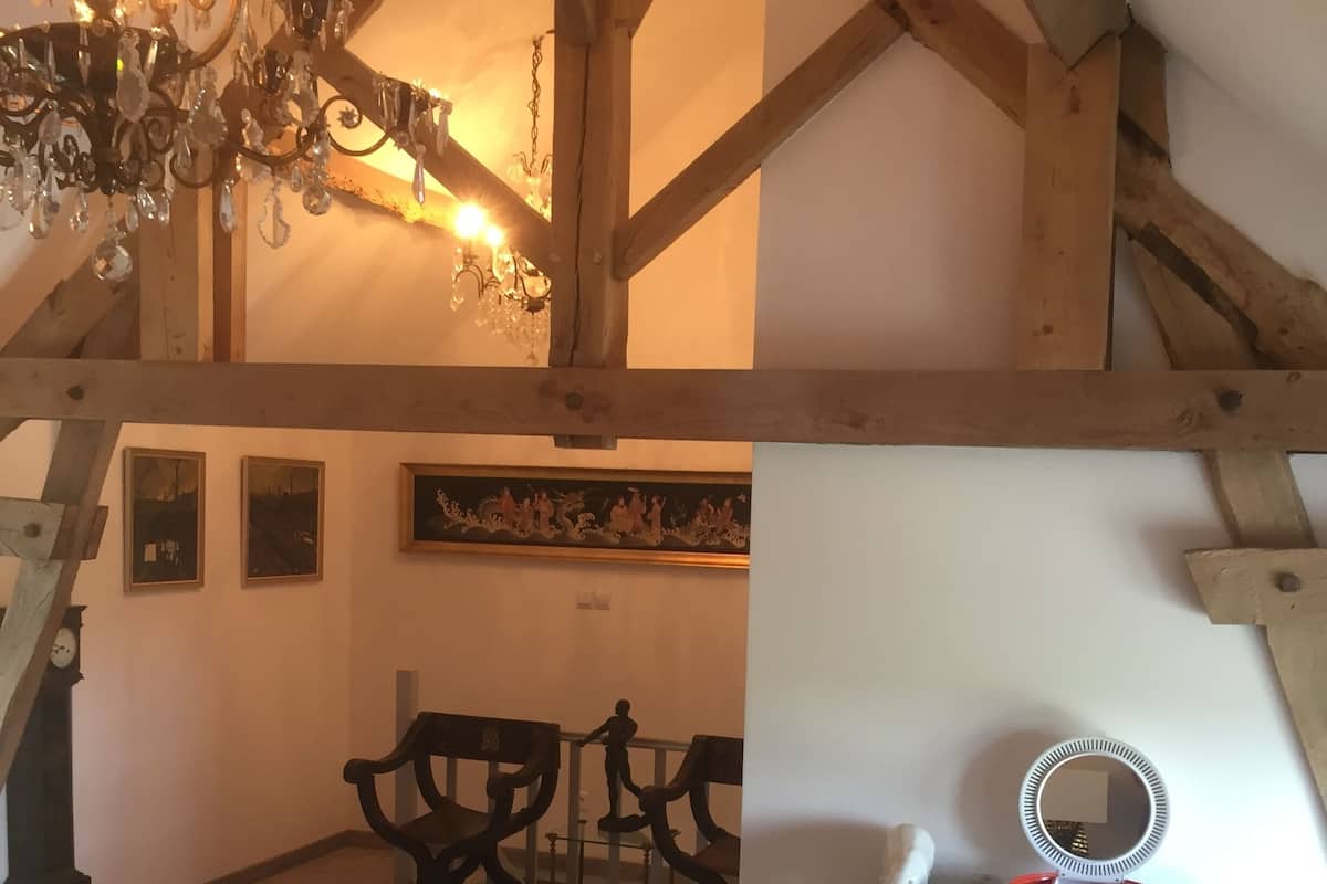 Ein rustikaler Raum mit sichtbaren Holzbalken, einer Kristallleuchtre, einem runden Spiegel und einem Gemälde an der Wand.