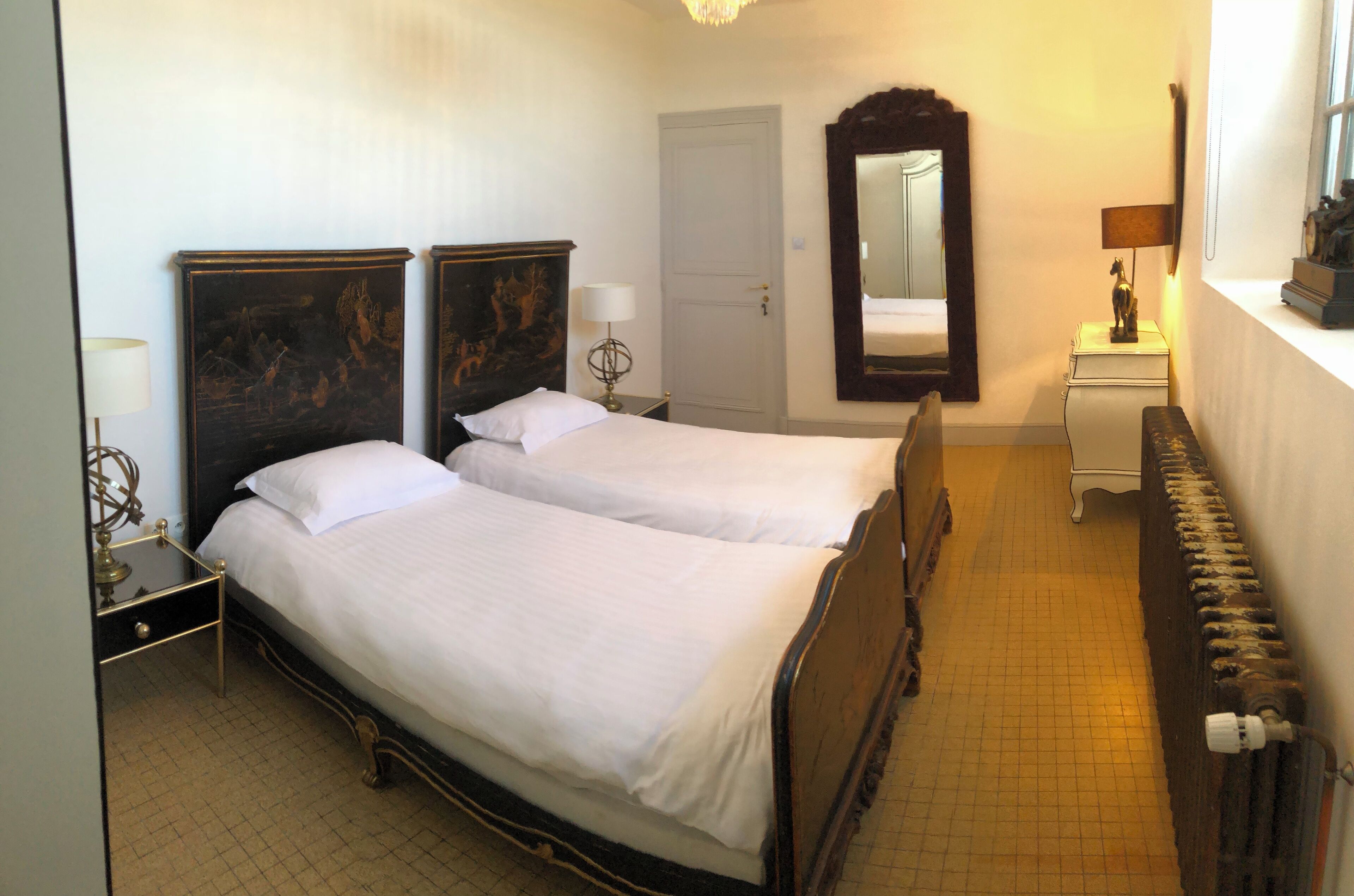 A hotel room with two beds, a large mirror, a dresser, and a radiator.