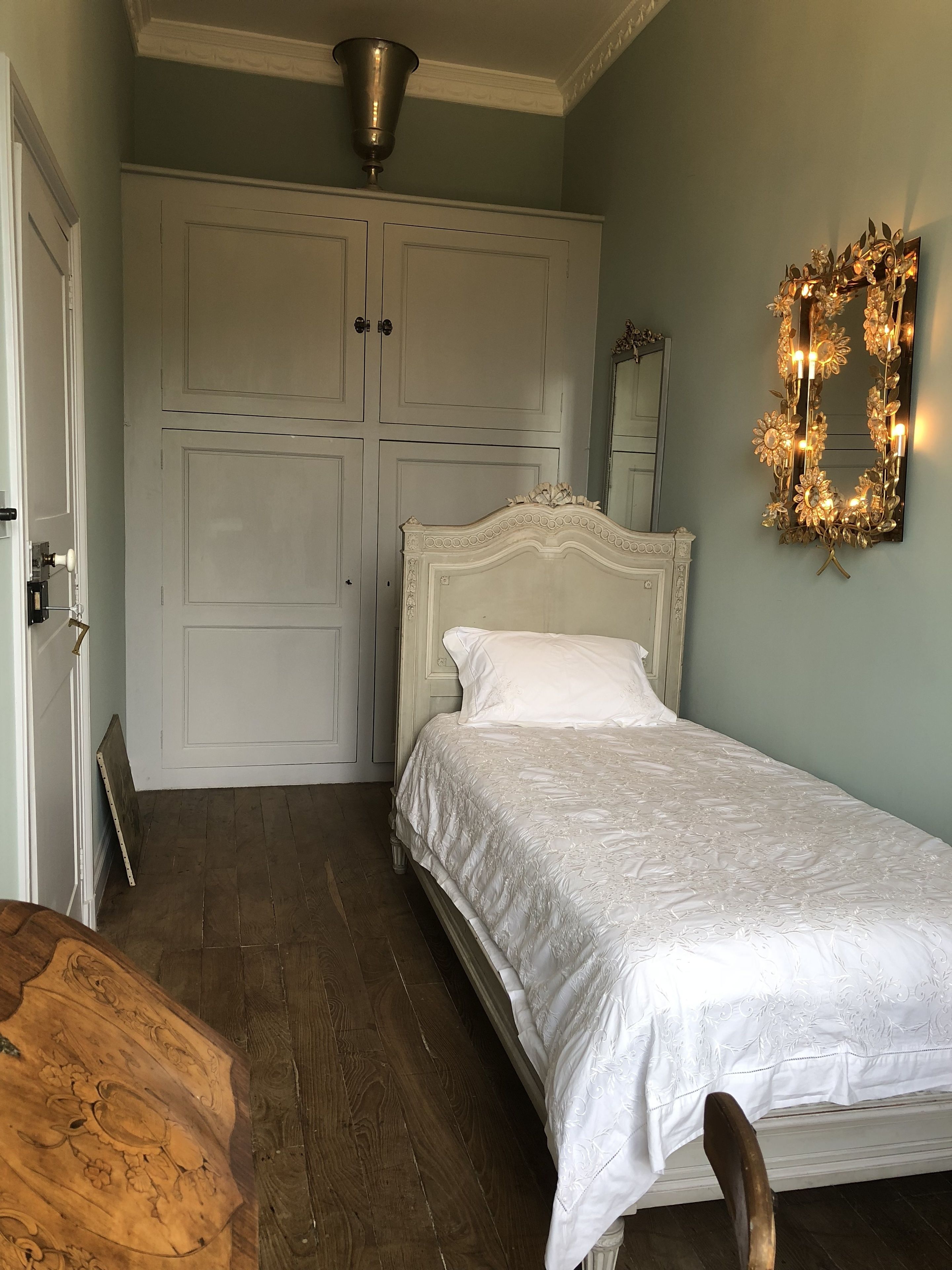 Un dormitorio con cama blanca, suelo de madera, armario blanco y espejo con luces.