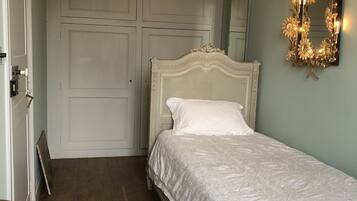 Un dormitorio con cama blanca, suelo de madera, armario blanco y espejo con luces.