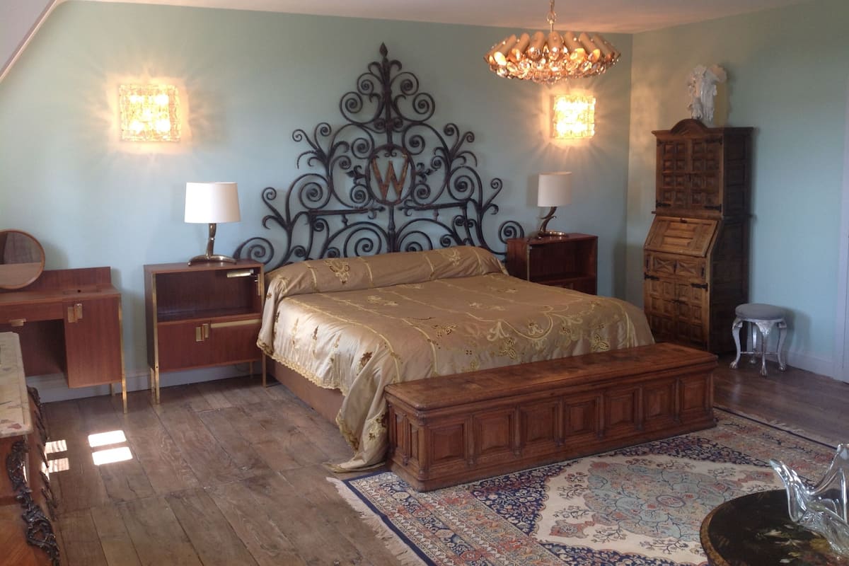 Ein Schlafzimmer mit einem großen Bett, Nachttischen aus Holz, einer Kommode und einer Chandelier.