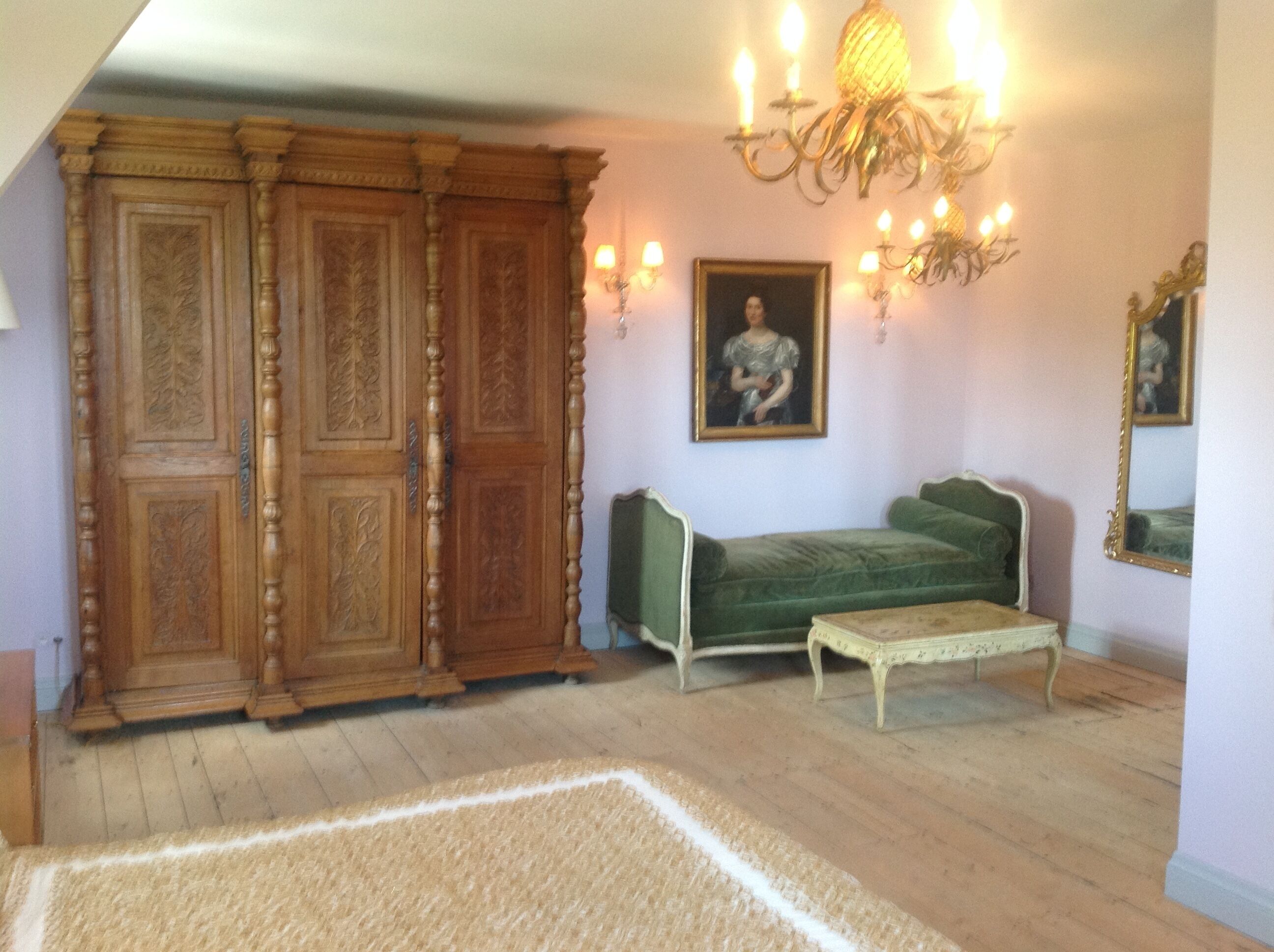 Een kamer met een groene bank, een houten kast, een tafeltje en een kroonluchter.