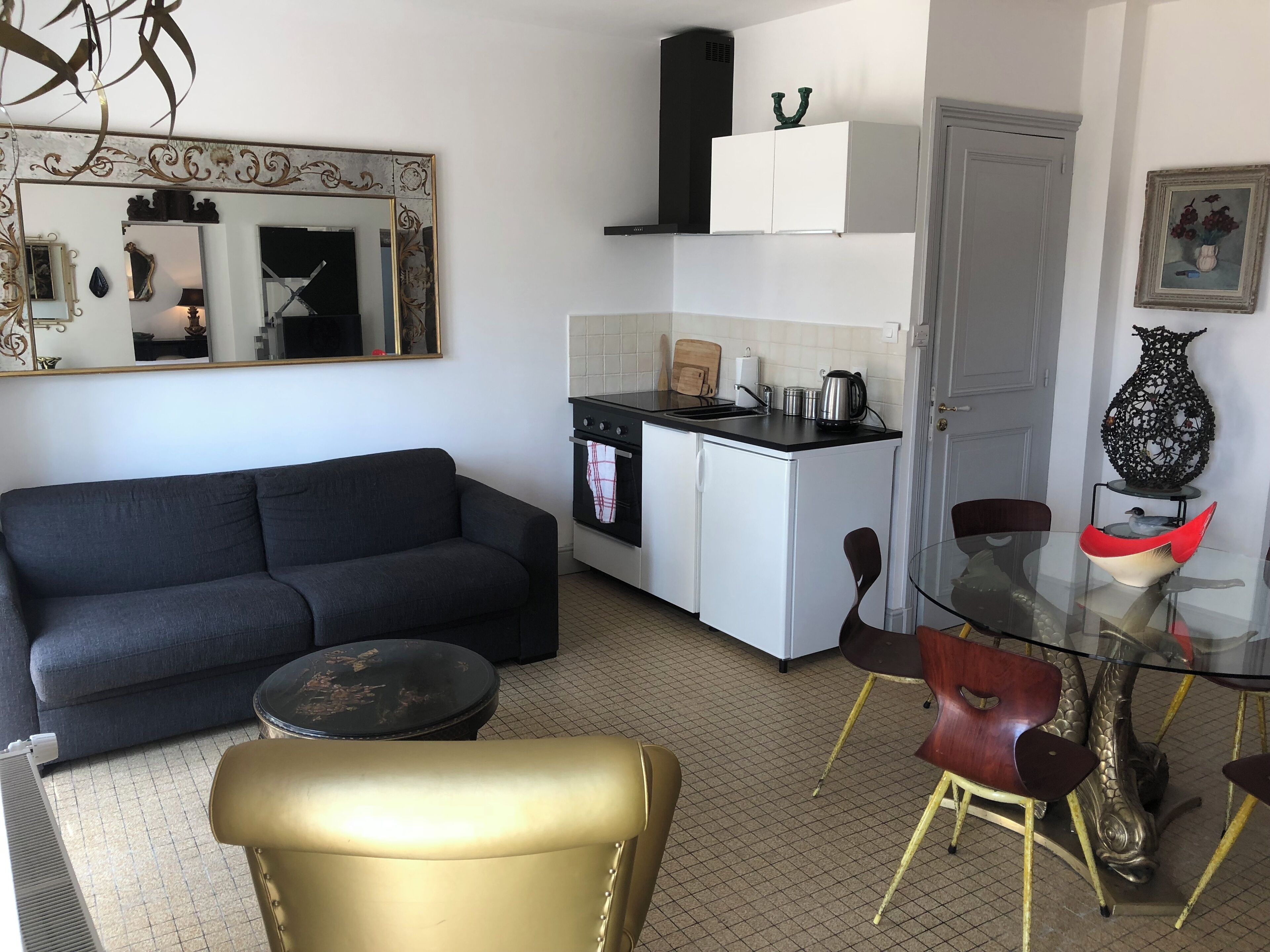 En kompakt opholdsstue med sofa, et lille tekøkken, et spisebord med stole og et dekorativt spejl.