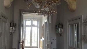 Un couloir orné d’un lustre, doté d’un grand miroir et d’une porte donnant sur une autre pièce.