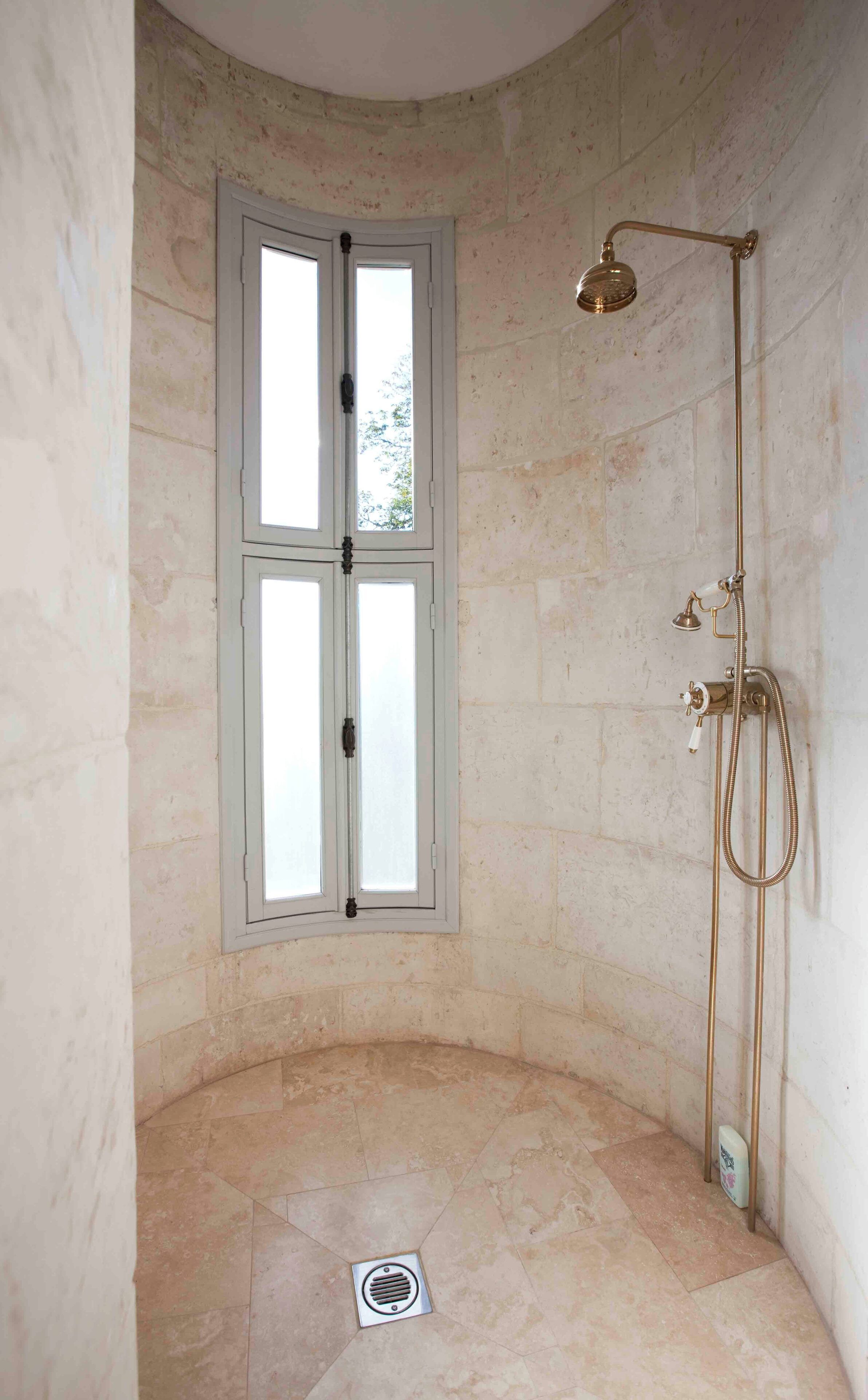 A shower room with a window, a showerhead, and a drain.