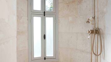 A shower room with a window, a showerhead, and a drain.