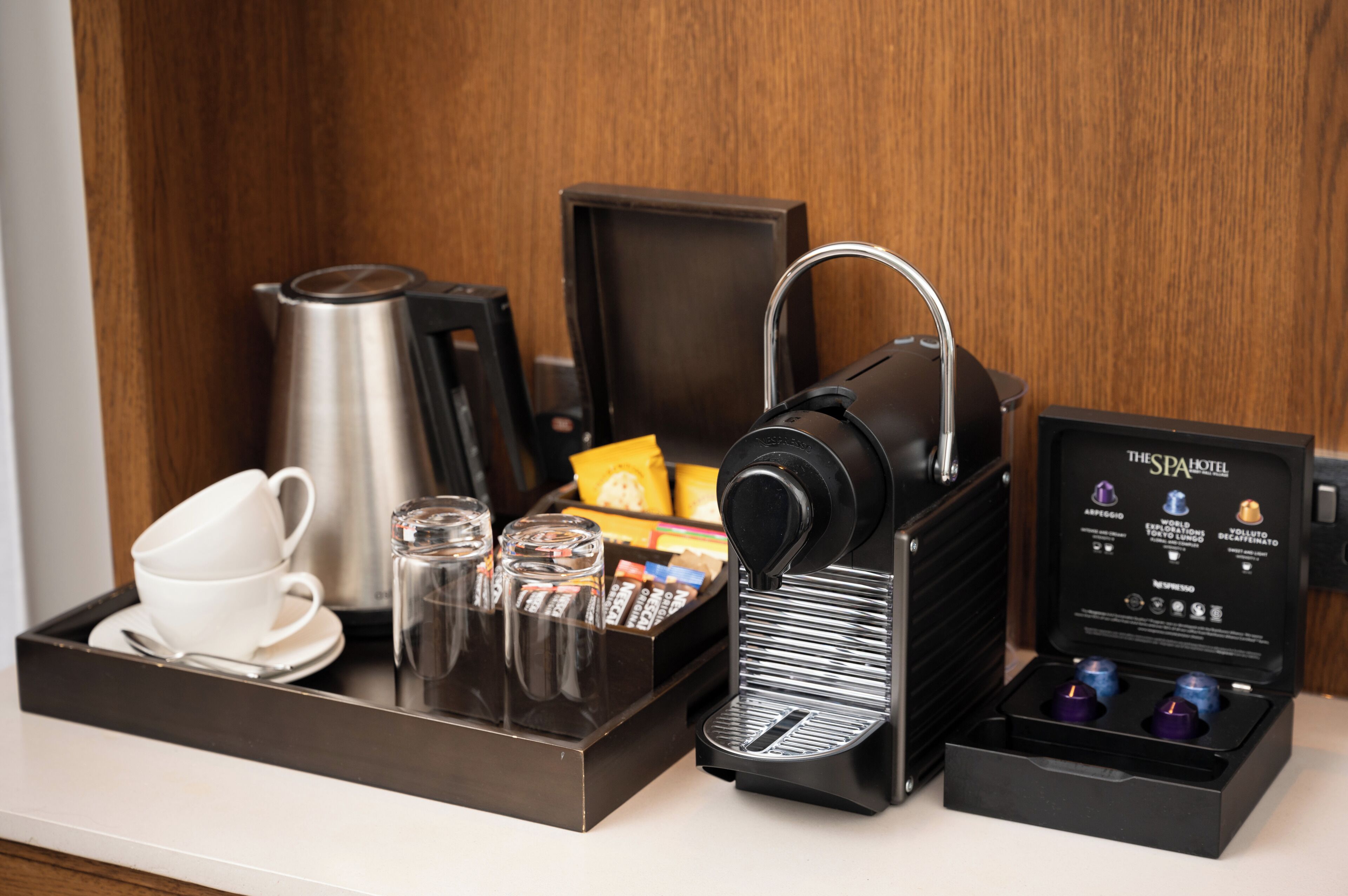 A coffee station with a coffee machine, cups, glasses, and a box of coffee pods.