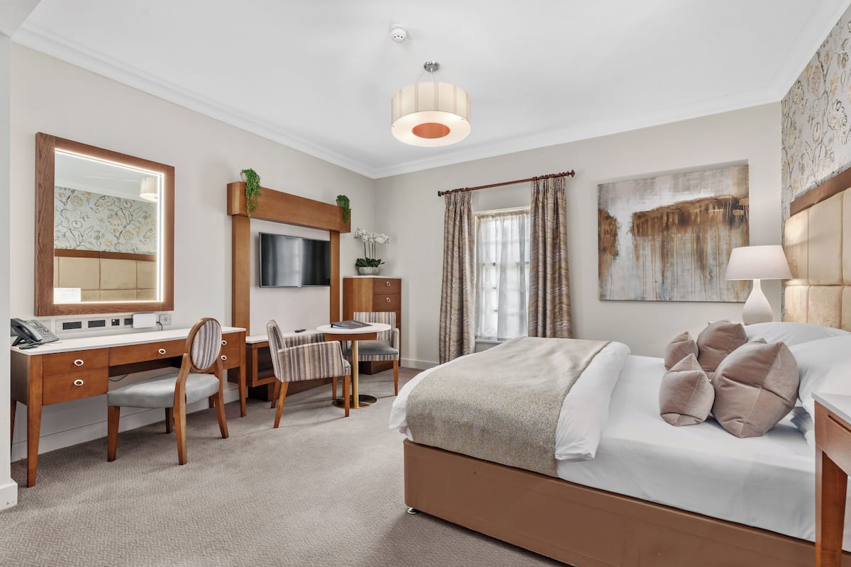 A hotel room with a bed, desk, chair, TV, and a large window with curtains.