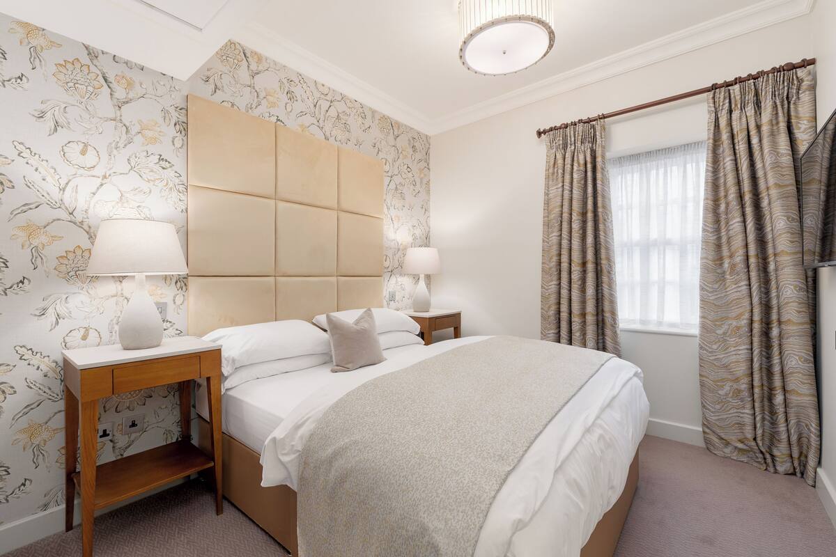 A neatly arranged bedroom with a large bed, two bedside tables with lamps, and a headboard.