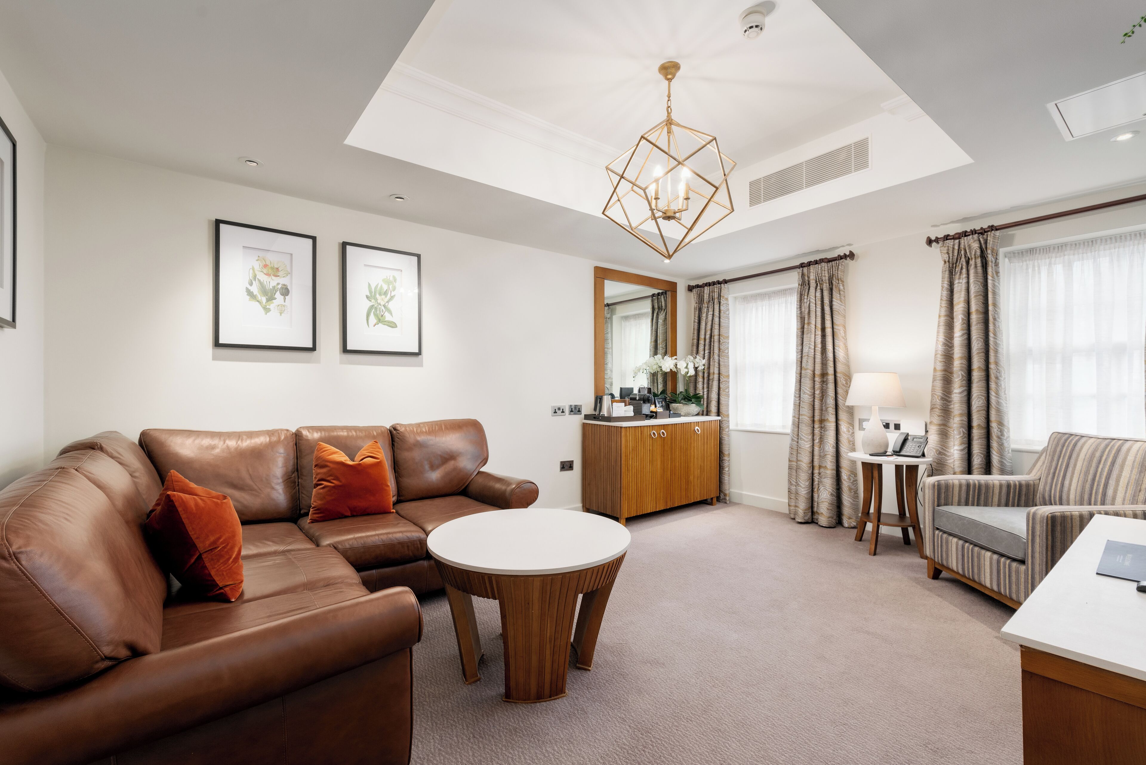 Un salon moderne avec un canapé en cuir marron, une table basse ronde en bois et un fauteuil à rayures. On y trouve également un meuble en bois et une petite table d’appoint avec une lampe.