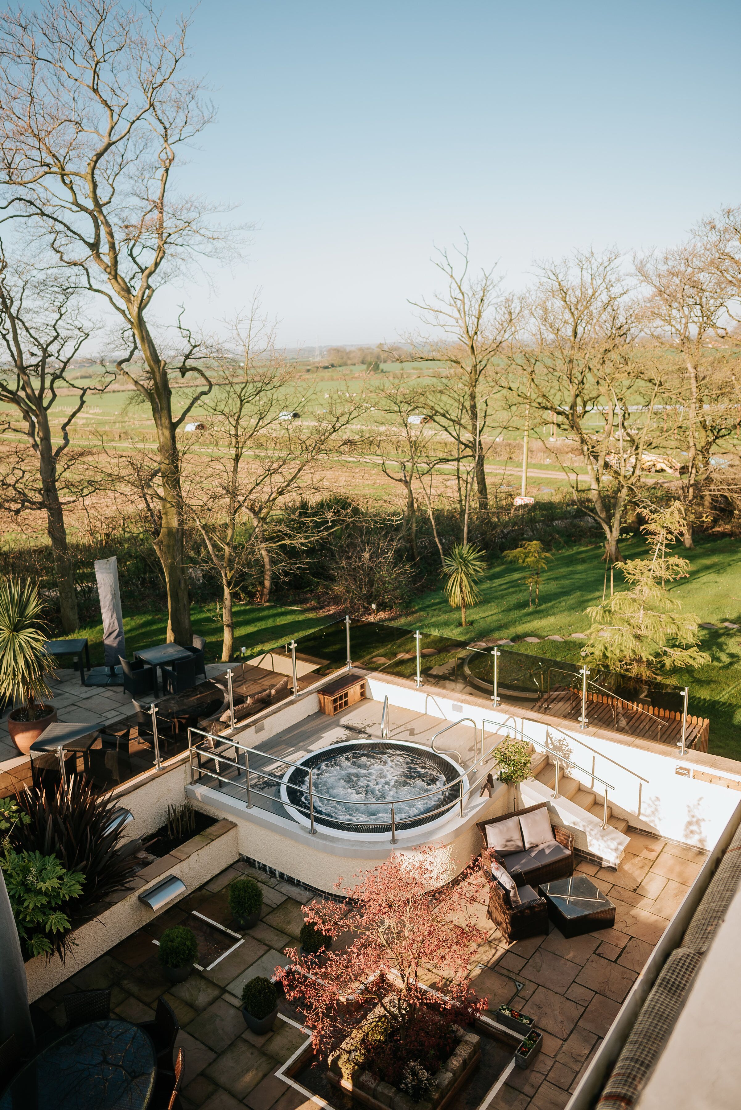 A patio area with a hot tub, outdoor furniture, and a view of a grassy field.