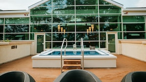 An outdoor swimming pool with a wooden deck, surrounded by wicker chairs, and a modern building with large glass windows in the background. - The Spa Hotel at Ribby Hall Village (Preston)