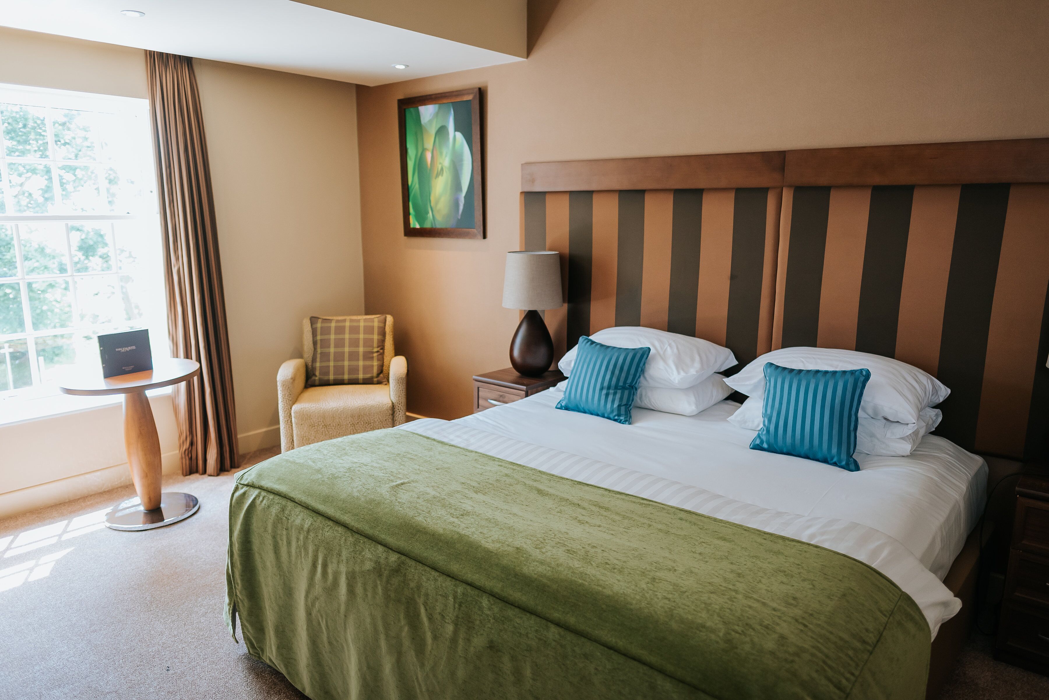 A hotel room with a large bed, a chair, a small table, and a lamp.