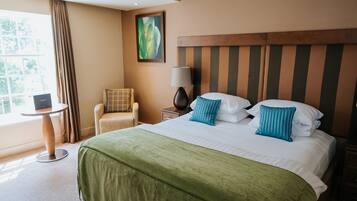 A hotel room with a large bed, a chair, a small table, and a lamp.