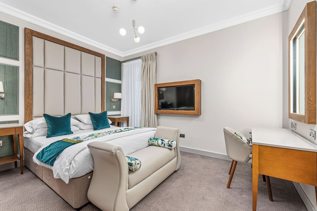 A hotel room with a bed, a sofa, a desk, and a TV.