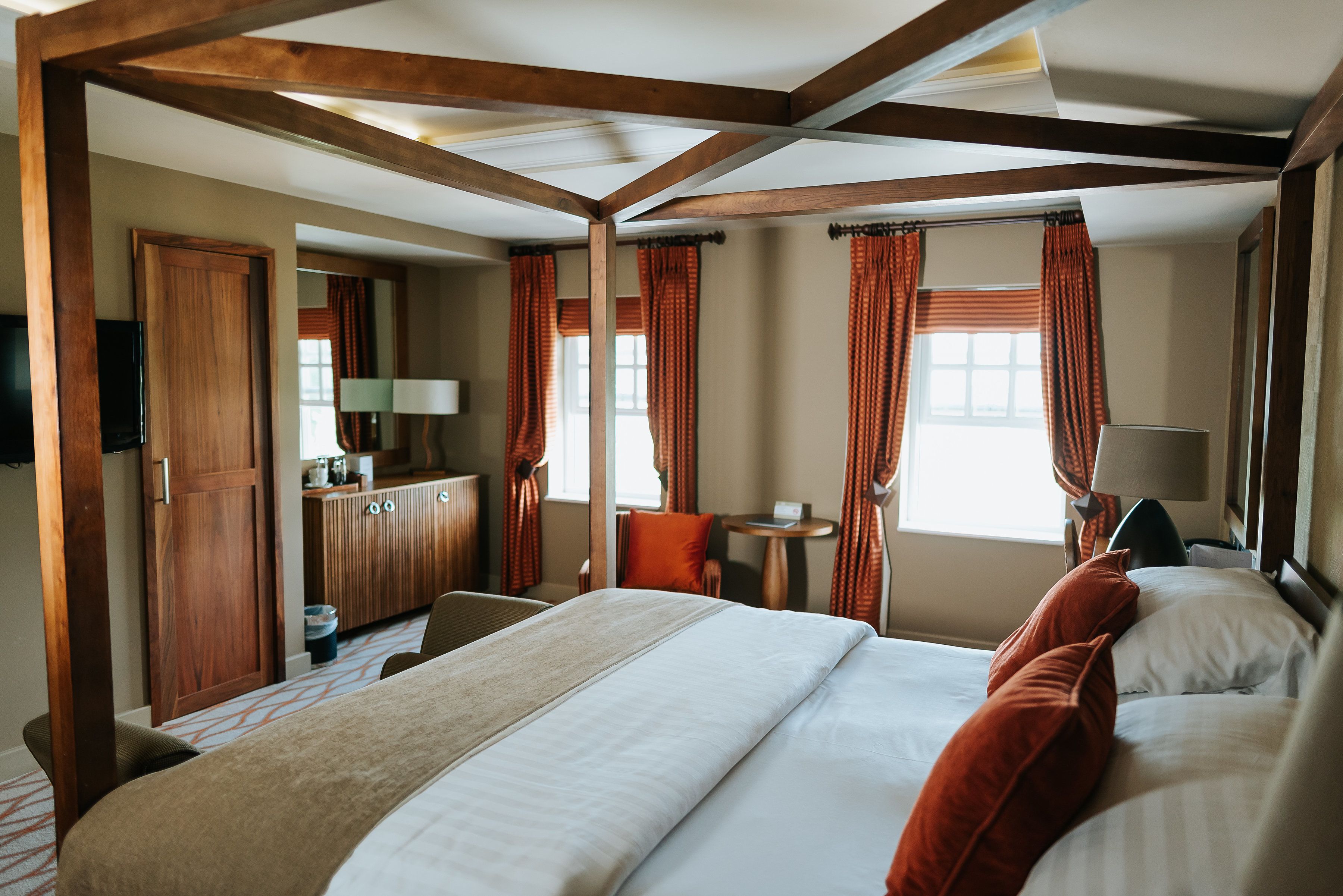 Ein Hotelzimmer mit einem großen Bett, einem Schreibtisch, einem Sessel, einem Fernseher und einem Fenster mit Vorhängen.