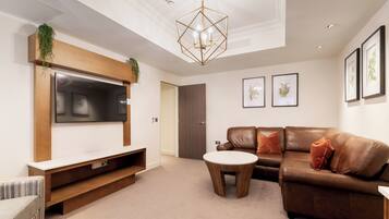 A modern living room with a flat-screen TV, a brown leather sofa, a round coffee table, and framed artwork on the walls.