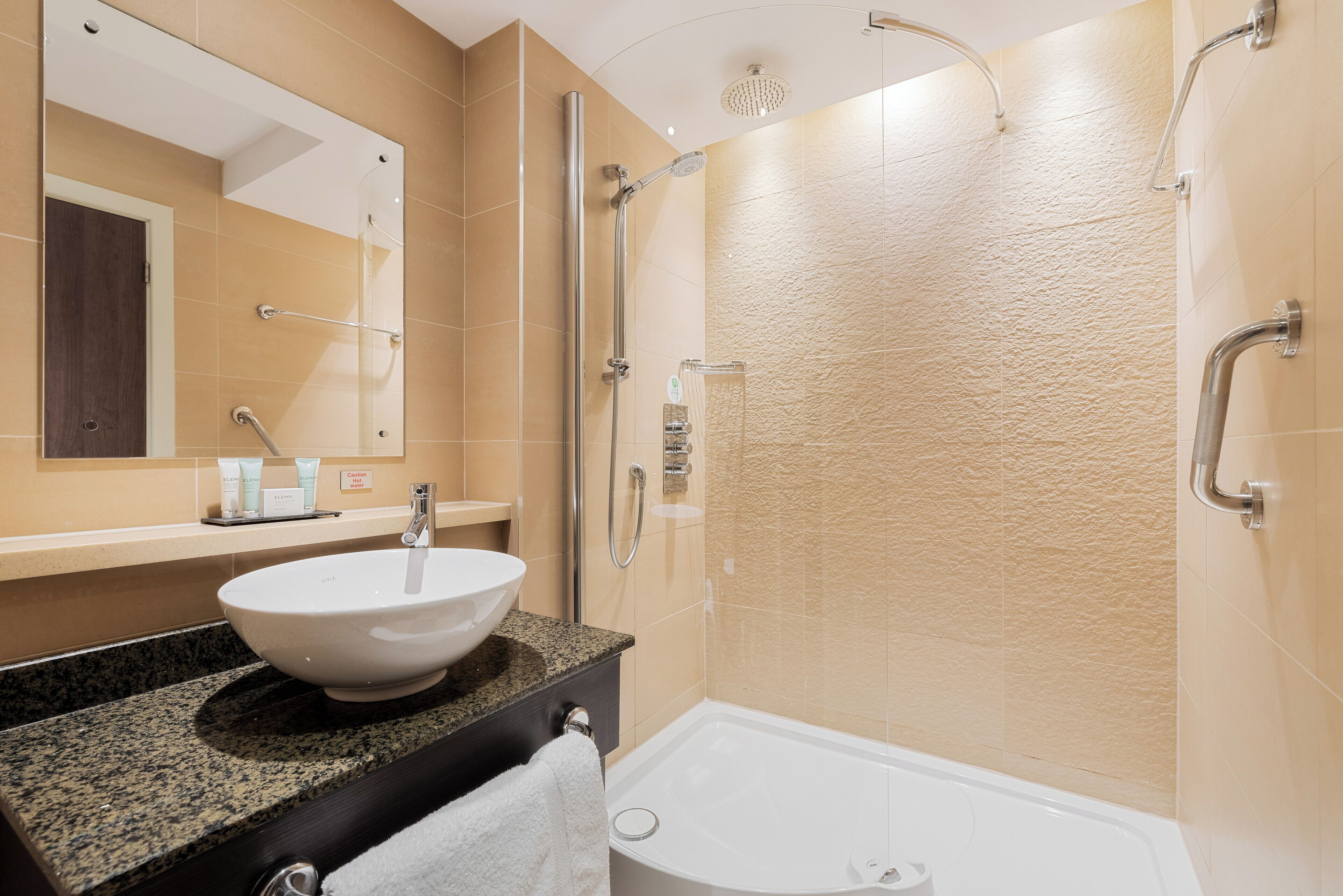 A modern bathroom with a granite countertop, a white sink, a glass-enclosed shower, and a bathtub.