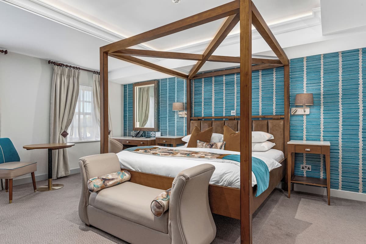 A four-poster bed with a wooden frame, a beige sofa, a small table, and a nightstand with a lamp.