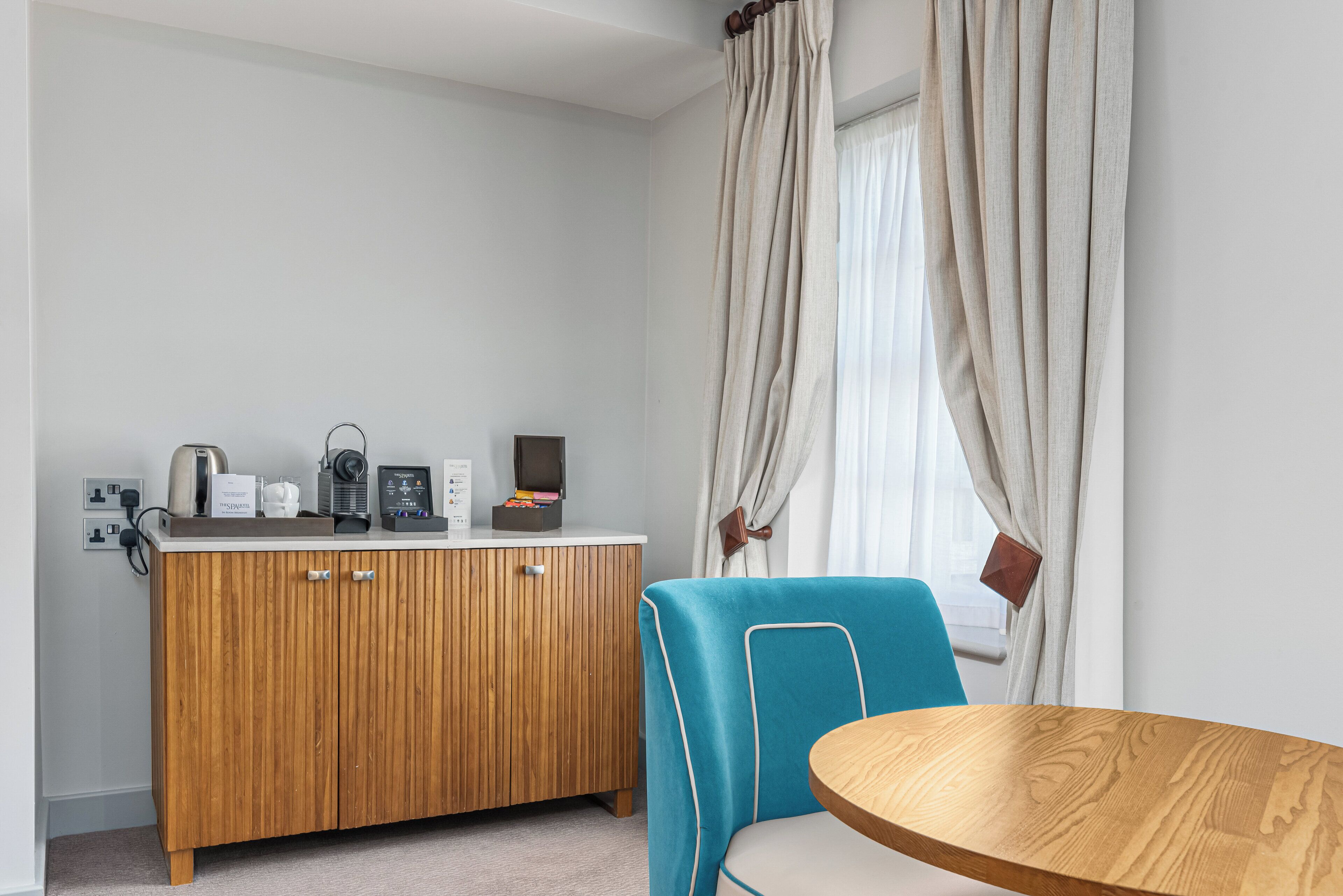 A room with a wooden cabinet, a blue chair, and a round wooden table.