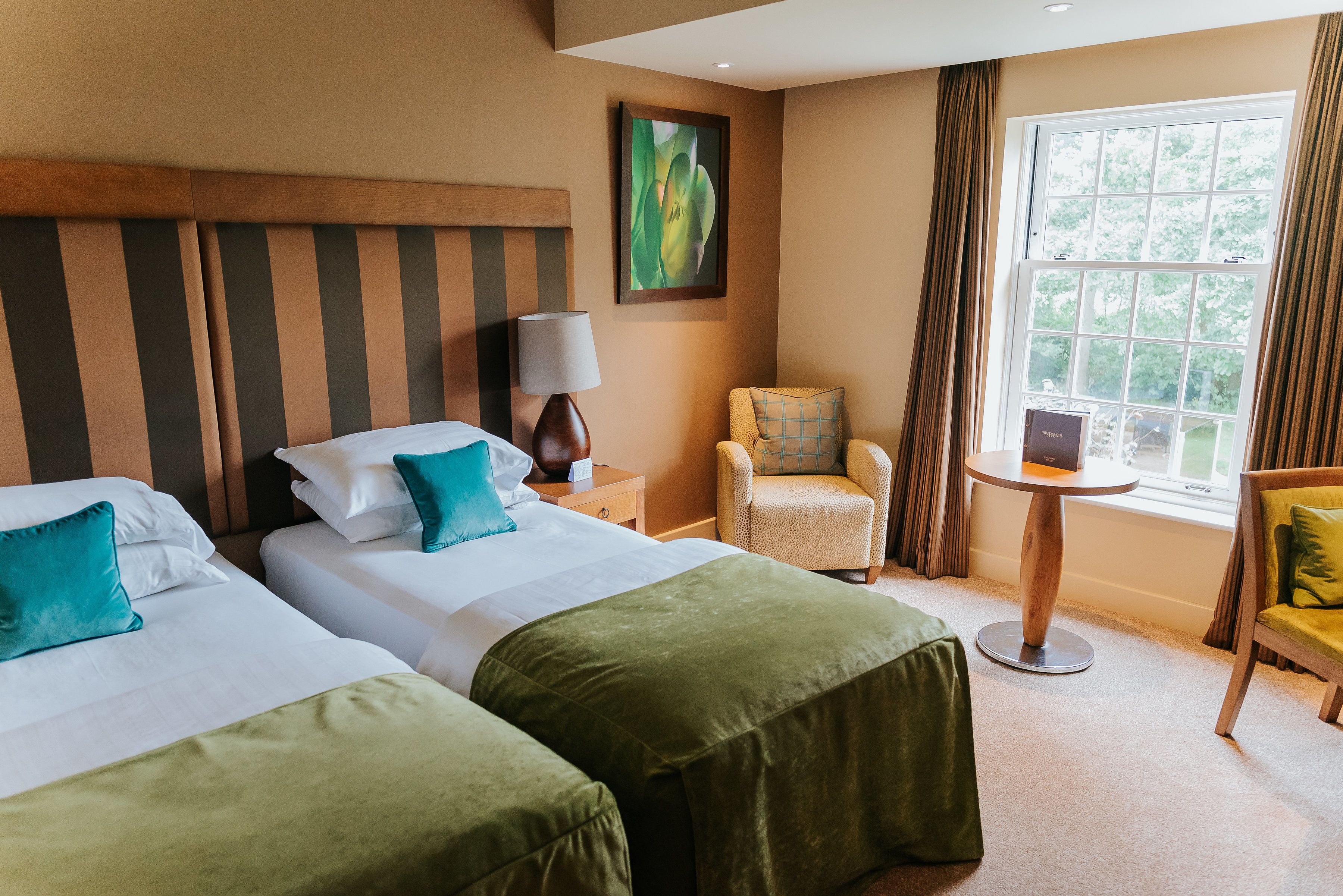 A hotel room with two beds, a chair, a table, and a window with curtains.