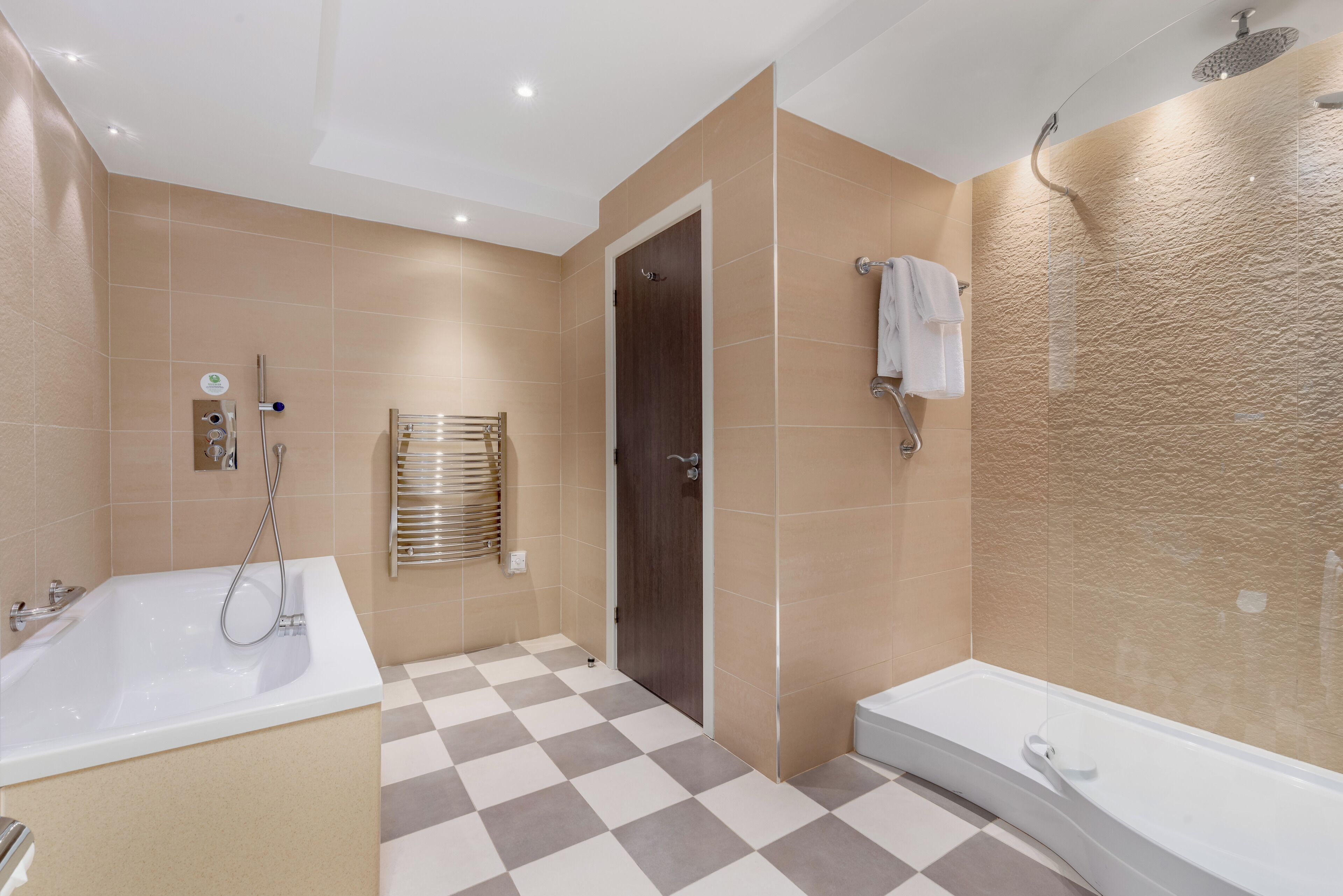 Un baño moderno con suelo a cuadros, una bañera, zona de ducha y un perchero para toallas.