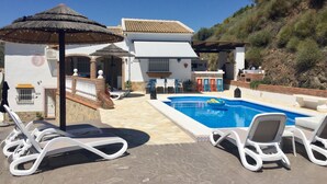 Zona de piscina amb gandules, un bar i un parasol de palla.