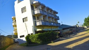 Un immeuble à plusieurs étages doté de balcons, une route de terre devant et une clôture le long du côté.