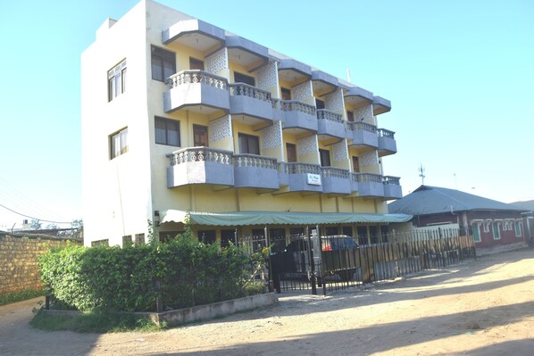 Un edificio de varios pisos con balcones, un acceso con portón y una zona techada donde se encuentra estacionado un automóvil.