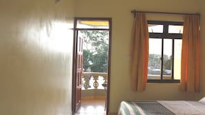 Une chambre à coucher avec un lit, une fenêtre avec des rideaux, un balcon avec une balustrade et une porte donnant sur l’extérieur.