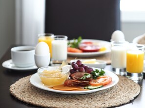 Ein gedeckter Frühstückstisch mit Eiern, Toast, Tomaten, Gurken und Käse. Dazu gibt es Gläser Orangensaft und Milch, eine Tasse Kaffee und eine Schale Obst.