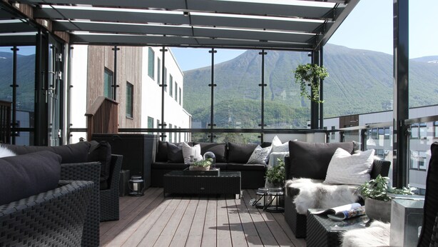 A modern outdoor seating area with wicker furniture, a central sofa, and a view of mountains.