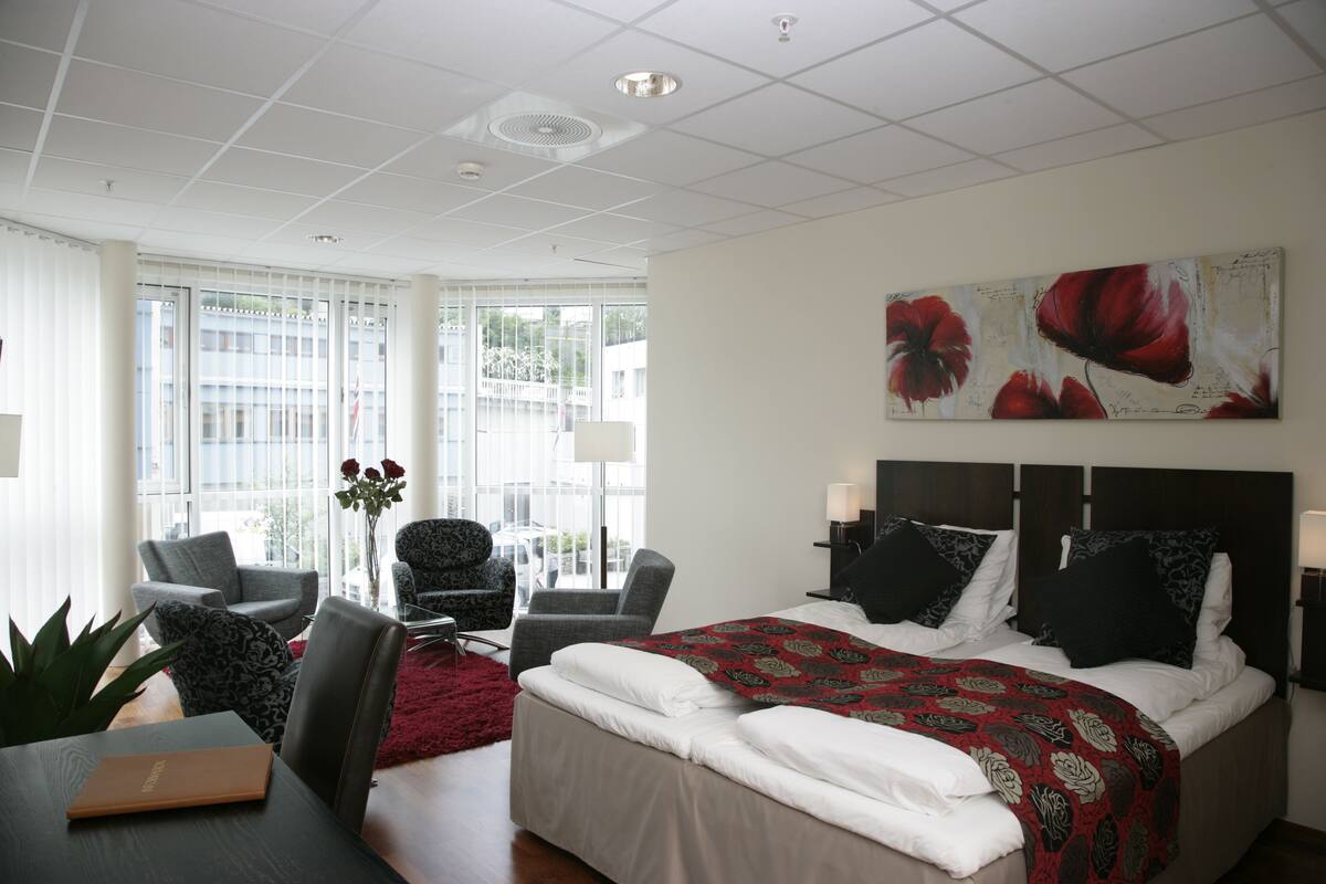 Ein Hotelzimmer mit einem großen Bett, zwei Sesseln, einem Schreibtisch und einem roten Teppich.