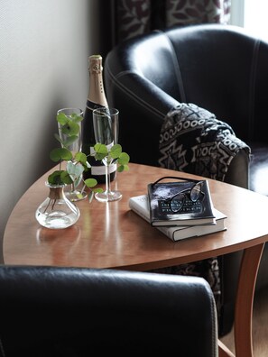 Ein Holztisch mit einer Champagnerflasche, zwei Gläsern und einem Buch, auf dem eine Brille liegt.