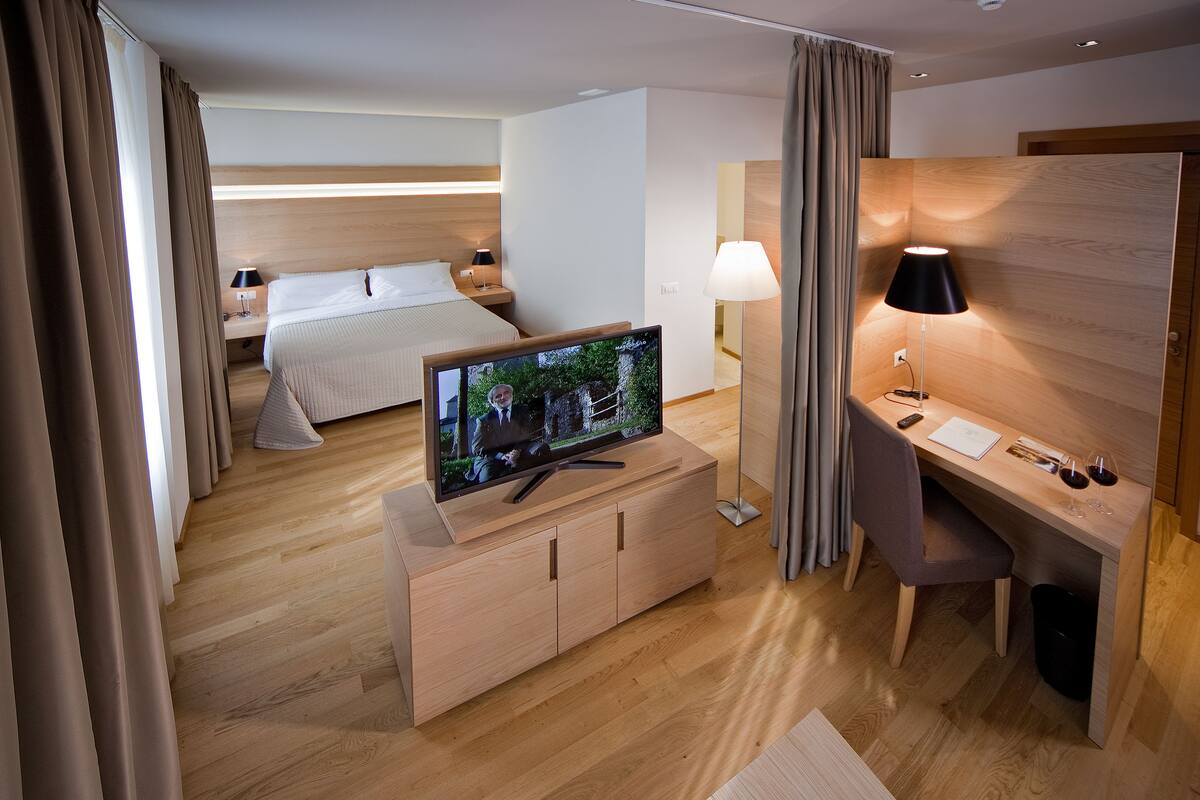 Une chambre d’hôtel moderne, équipée d’un lit, d’un téléviseur posé sur une console en bois, d’un bureau avec une lampe et offrant une vue sur l’extérieur.