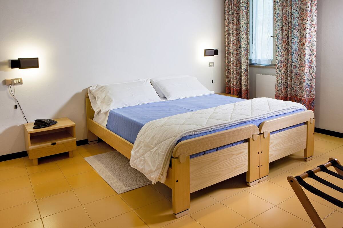 Un lit simple avec un cadre en bois, une table de chevet avec une lampe et une fenêtre avec des rideaux.