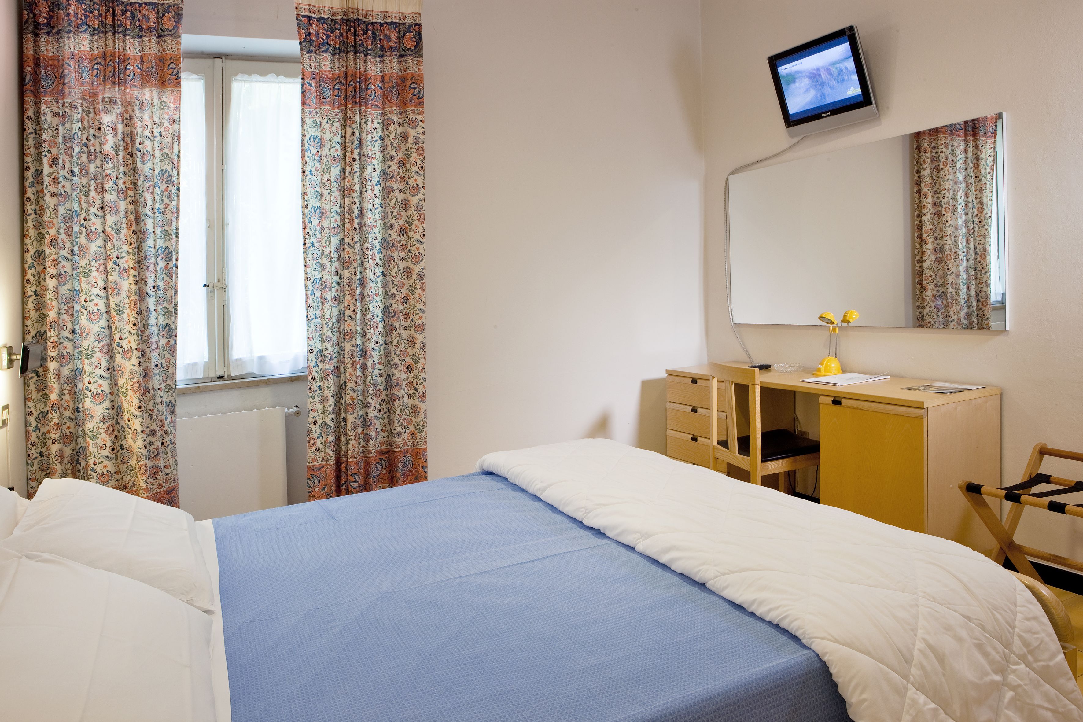 Ett hotellrum med en säng, ett skrivbord, en stol, en spegel och en tv.