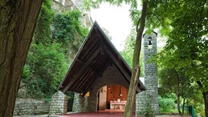Une chapelle en pierre, avec un toit en bois et un clocher, entourée d’arbres.