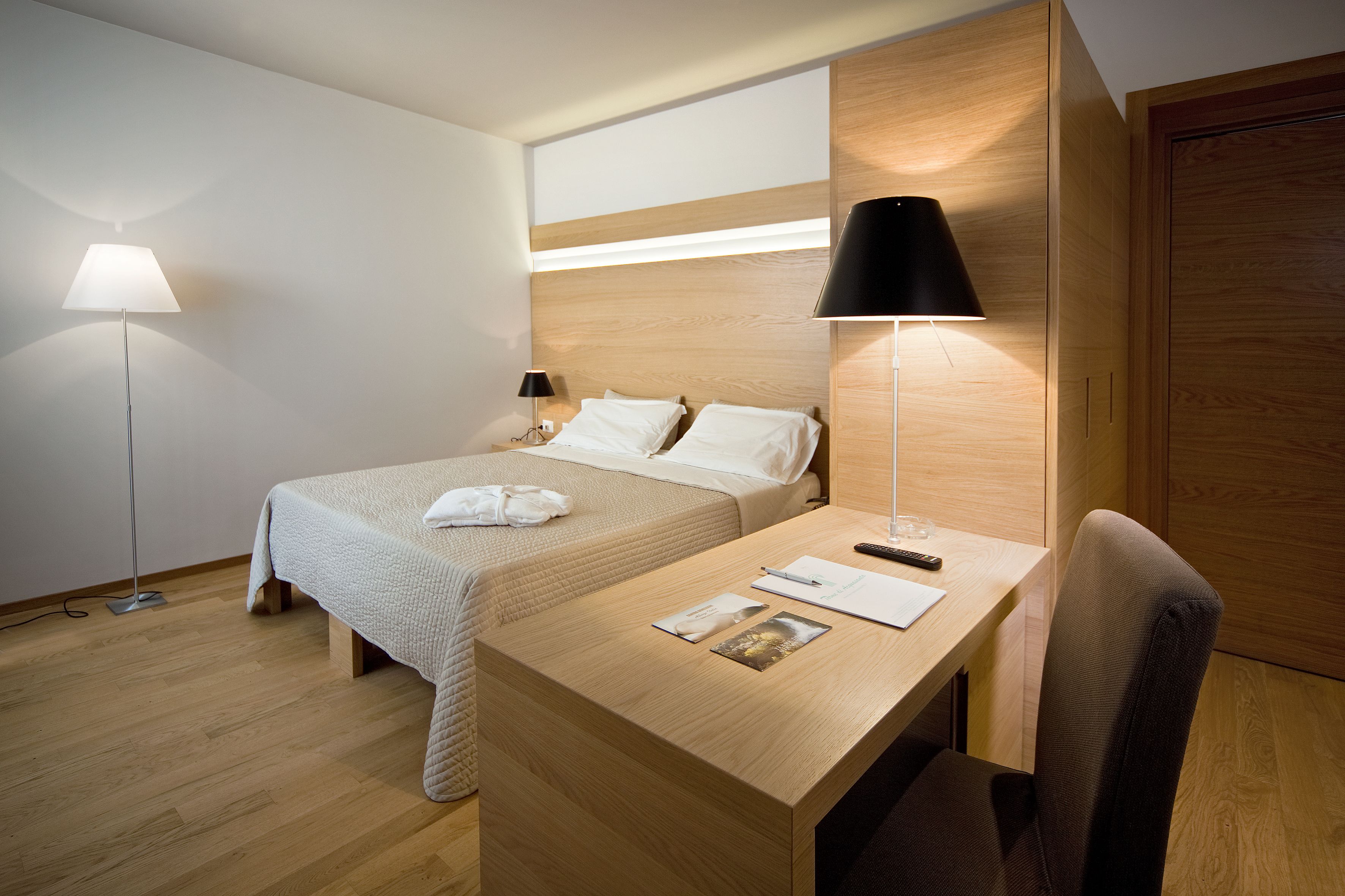 Una habitación de hotel con cama, mesita de noche, escritorio, silla y dos lámparas.