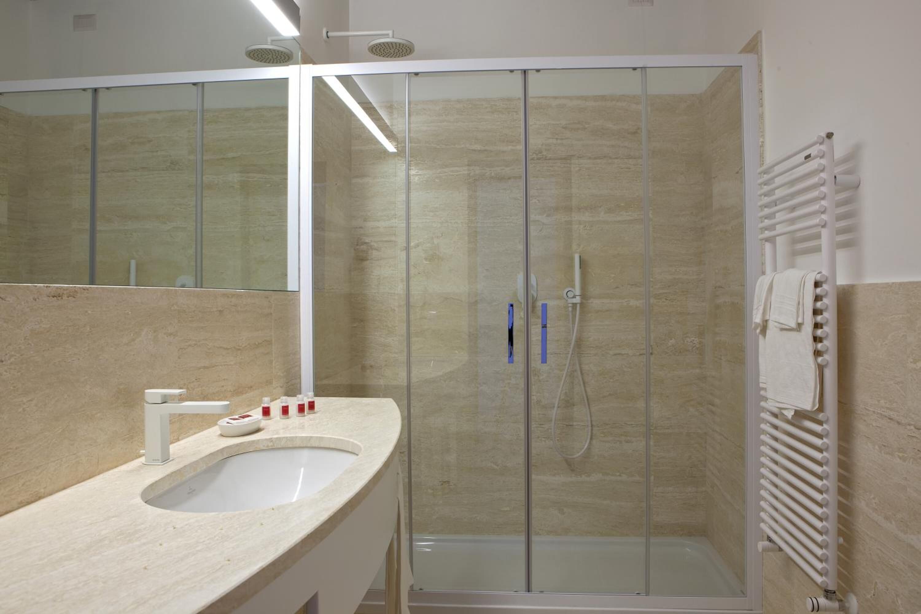 A modern bathroom with a glass-enclosed shower, a sink with toiletries, and a towel rack.