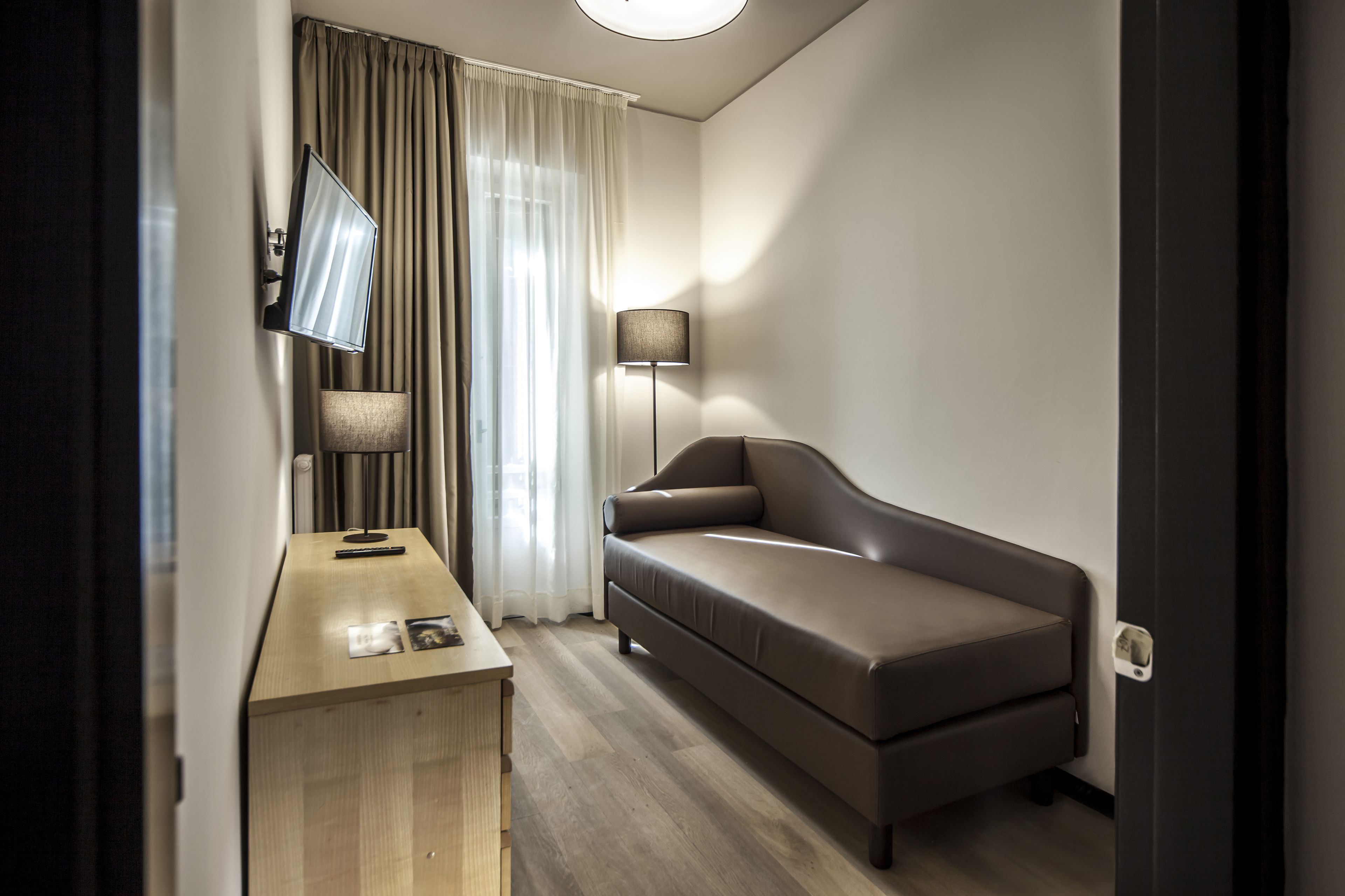 Quarto de hotel moderno com escrivaninha de madeira, sofá, TV de tela plana e abajur.
