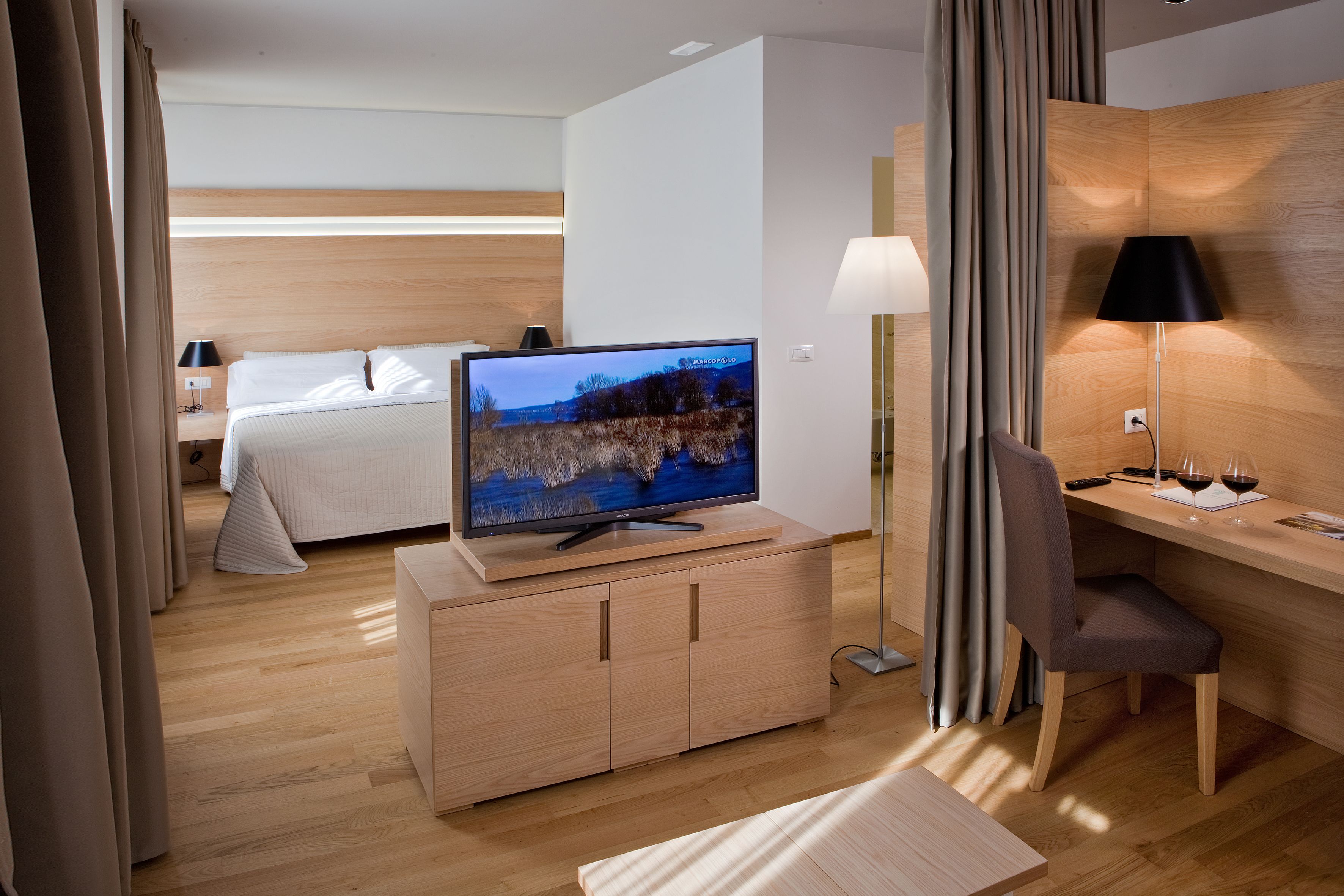 Ett hotellrum med en säng, en tv-apparat på ett träskåp, ett skrivbord med en stol och en lampa.