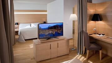 Ett hotellrum med en säng, en tv-apparat på ett träskåp, ett skrivbord med en stol och en lampa.